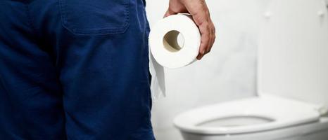 mann leidet an durchfall hand hält seidenpapierrolle vor toilettenschüssel. verstopfung im badezimmer. Behandlung von Magenschmerzen und Hygiene, Gesundheitsversorgung foto