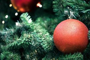 Nahaufnahme einer roten Kugel, die an einem geschmückten Weihnachtsbaum hängt, auf verschwommenen Lichtern mit geschmücktem Baum, funkelnden und bokeh Hintergrund. Kopieren Sie Platz für Ihren Text. foto