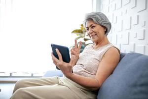 asiatische Seniorin mit Smartphone für Videoanrufe mit fröhlicher Stimmung lächelnd und lachend auf dem Sofa zu Hause. foto