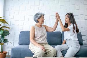 asiatische großmutter und enkelin sprechen und hallo-five zu hause. Senior und junge Frau lächelnd und fröhliche Stimmung auf dem Sofa im Wohnzimmer. foto