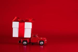 rotes Auto mit einer Geschenkbox auf rotem Grund. konzept - lieferung von geschenken für die feiertage, valentinstag, internationaler frauentag, 14. februar, 8. märz. einkaufen, verkauf foto