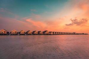 sonnenuntergang auf der malediveninsel, luxuriöses wasservillenresort und holzsteg. atemberaubender himmel und wolken und strandhintergrund für sommerferienurlaub und reisekonzept. erstaunliche sonnenaufgang tropische landschaft foto