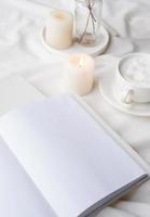 weißes leeres buch mit tasse kaffee und brennender kerze, gemütliche komposition mit geöffnetem buchmodell foto