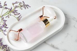 Kosmetisches ätherisches Rosenöl und Rosenquarz-Gesichtsmassagegerät für die Schönheitsmassage des Gesichts zu Hause. Hautpflege- und Gesichtsbehandlungskonzept. foto