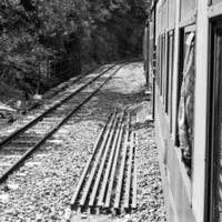 spielzeugeisenbahn, die sich am berghang bewegt, schöne aussicht, eine seite des berges, eine seite des tals, die auf der eisenbahn zum hügel fährt, inmitten grüner naturwälder. spielzeugeisenbahn von kalka nach shimla in indien-schwarz und weiß foto