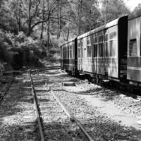 spielzeugeisenbahn, die sich am berghang bewegt, schöne aussicht, eine seite des berges, eine seite des tals, die auf der eisenbahn zum hügel fährt, inmitten grüner naturwälder. spielzeugeisenbahn von kalka nach shimla in indien-schwarz und weiß foto