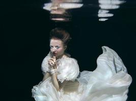 junge Frau im langen weißen Luxuskleid unter Wasser auf dem schwarzen Hintergrund. bewegung, kunst, winterkonzept foto