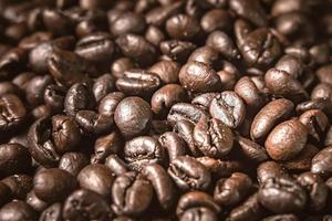 Kaffee auf hölzernem Hintergrund. braune geröstete Kaffeebohnen, Samen auf dunklem Hintergrund. Espresso dunkel, Aroma, schwarzes Koffeingetränk. Nahaufnahme isolierter Energiemokka, Cappuccino-Zutat. foto