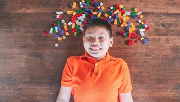 asiatische kinder legen sich auf holzböden, spielen mit bunten plastikklötzchen und haben spaß beim bauen und gestalten zu hause. foto