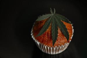 Cannabis-Lebensmittelkuchen mit Cannabisblatt-Marihuana-Kraut auf dunklem Hintergrund, köstliche süße Dessert-Cupcakes mit Hanfblattpflanze thc cbd-Kräuter-Food-Snack und medizinisches Konzept foto