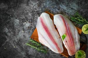 Fischfilet auf Holzbrett mit Zutaten zum Kochen, Fleisch Dolly Fisch Tilapia gestreifter Wels, frisches rohes Pangasius Fischfilet mit Kräutern und Gewürzen schwarzer Pfeffer Zitrone Limette foto