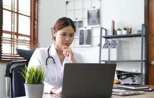 Portrait glückliche asiatische Ärztin, Telemedizin-Konzept. asiatische Ärztin spricht mit Patientin über Laptop-Online-Video-Webinar-Konsultation, während sie im Klinikbüro sitzt