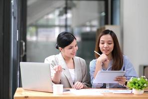zwei junge asiatische geschäftsfrauen diskutieren mit der ideenpräsentation eines neuen startup-projekts, analysieren planungs- und finanzstatistiken sowie den investitionsmarkt im büro. foto
