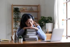 lächelnde asiatische Studentin im Grundstudium in der Bibliothek mit Laptop-Büchern, die Online-Recherchen für Kursarbeiten durchführen, Notizen für Aufsatz-Hausaufgaben machen, Online-Bildungs-E-Learning-Konzept foto