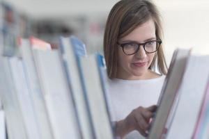 Porträt einer Studentin, die ein Buch zum Lesen in der Bibliothek auswählt foto