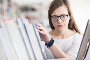 Porträt einer Studentin, die ein Buch zum Lesen in der Bibliothek auswählt foto