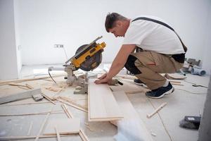 Mann schneidet Laminatdiele mit elektrischer Kreissäge foto