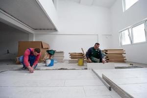 Arbeiter, die die keramischen Fliesen in Holzoptik auf dem Boden verlegen foto