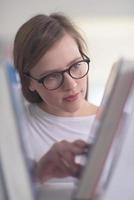 Porträt einer Studentin, die ein Buch zum Lesen in der Bibliothek auswählt foto