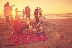 Paar genießt mit Freunden den Sonnenuntergang am Strand foto