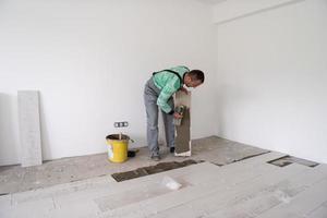 Arbeiter, der die Keramikfliesen in Holzoptik auf dem Boden installiert foto