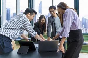 ein team junger asiatischer unternehmer hat ein kleines teammeeting für ein bevorstehendes projekt für marketing- und verkaufsmanagement mit wolkenkratzeransicht für ein gründungs- und bildungskonzept foto