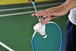 Badmintonspieler hält Schläger und Federball mit weißer Creme vor das Netz, bevor er ihn auf einer anderen Seite des Platzes serviert. foto