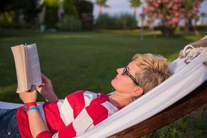 Frau, die ein Buch liest, während sie sich auf der Hängematte entspannt foto