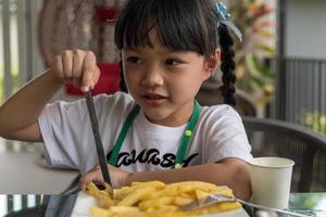 Junges asiatisches Mädchen, das Pommes frites isst, junges Kind, Spaß, glücklich, Kartoffel-Fast-Food. foto