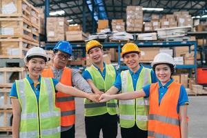 gruppe von asiatischen arbeitern im industrielager in der sicherheitssuite handstapel feiern erfolgreiches oder deal-engagement. logistik, lieferkette und lagergeschäft. teamwork-einheit unter sichtkonzept. foto