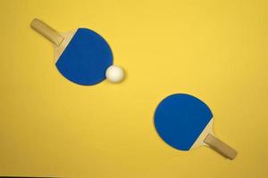 Zwei blaue Tischtennisschläger liegen auf gelbem Grund foto