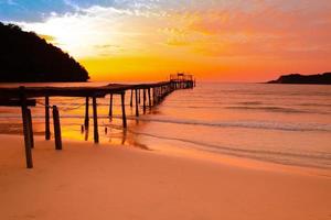 Meerblick-Sonnenuntergang mit einem hölzernen Pier, der sich bis zum Meer und bewölktem Himmel erstreckt, um im Sommer im Urlaub zu entspannen foto