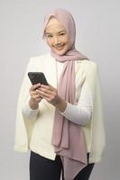 Schöne muslimische Frau mit Hijab mit Smartphone auf weißem Hintergrund, Technologiekonzept. foto