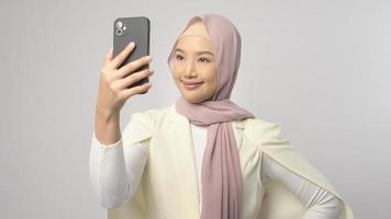 Schöne muslimische Frau mit Hijab mit Smartphone auf weißem Hintergrund, Technologiekonzept. foto