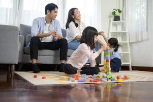 asiatische familie mit kindern, die spielen und turm aus bunten holzspielzeugblöcken im wohnzimmer zu hause bauen, lernspiel. foto