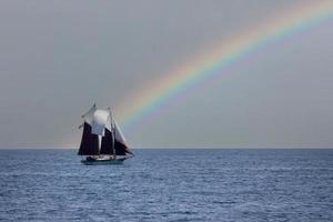 altes segelboot, das auf regenbogenhimmelhintergrund segelt foto