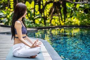 Frau, die Yoga und Meditation in einer Lotus-Yoga-Position am blauen Swimmingpool trainiert foto