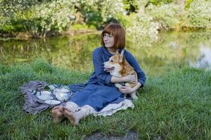 junge frau im retro-kleid mit lustigem corgi-hund auf dem picknick, frau mit süßem hund trinkt englischen tee im park foto