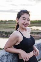 asiatische Frau, die sich nach dem Joggen bei Sonnenuntergang auf einer Brücke entspannt. foto