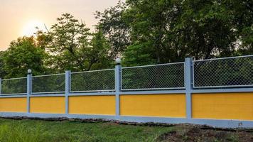 Gelber Betonwandzaun mit Stahlgitter im Waldgarten. foto