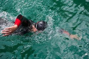 Triathlon-Athlet, der auf dem See schwimmt und einen Neoprenanzug trägt foto