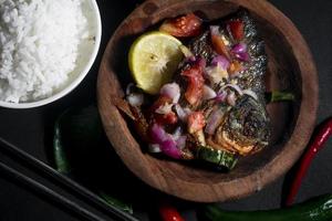 würziges gebratenes Fischmenü mit Reisschüssel auf schwarzem Hintergrund. asiatische Lebensmittelfotografie. gut für Speisekarte und Poster