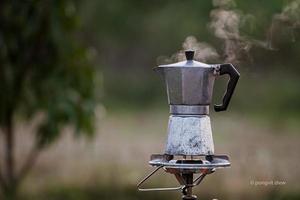 antike kaffee-moka-kanne auf dem gasherd zum camping, wenn die sonne morgens aufgeht. weicher fokus.