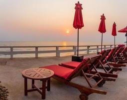 Roter Sonnenschirm und Liegestühle bei Sonnenaufgang rund um den Außenpool. foto