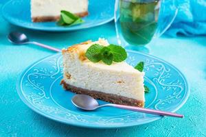 geschnittener Käsekuchen. köstlicher süßer Käsekuchen mit Pfefferminztee auf blauem Hintergrund foto