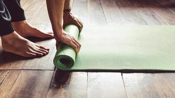 Nahaufnahme eines Mannes, der eine grüne Yogamatte oder Trainingsmatte von Hand rollt, nachdem er morgens Wellness-Yoga-Praxis zu Hause trainiert hat. gesundes leben und gesundes wohnkonzept. foto