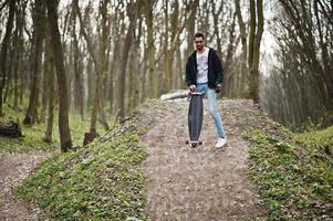 arabischer Streetstyle-Mann mit Brille und Longboard auf Holz. foto