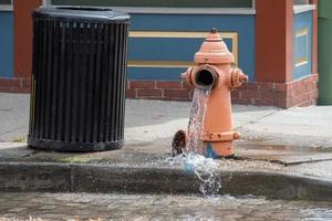 Straße orangefarbener Hydrant, der Wasser auf der Straße verteilt foto