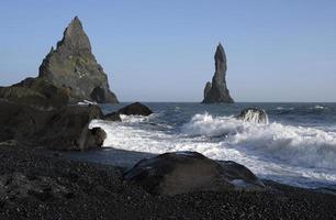 Wellen am schwarzen Strand von Reynisfjara, Island, mit Felsformationen im Hintergrund foto