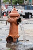 Straße orangefarbener Hydrant, der Wasser auf der Straße verteilt foto